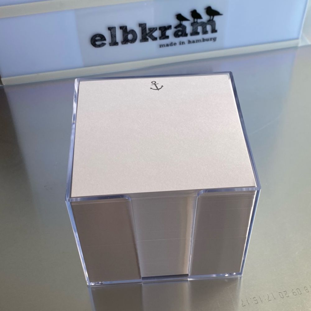 transparente Zettelbox aus Kunststoff für quadratische weissen Notizzetteln mit einem keinen grauen Anker mittig oben auf den Zettel