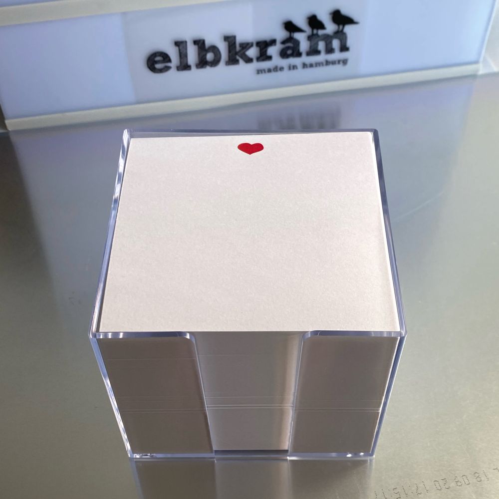 Transparente Zettelbox aus Kunststoff mit quadratischen Notizzetteln mit einem kleinen roten Herz mittig oben auf dem Zettel